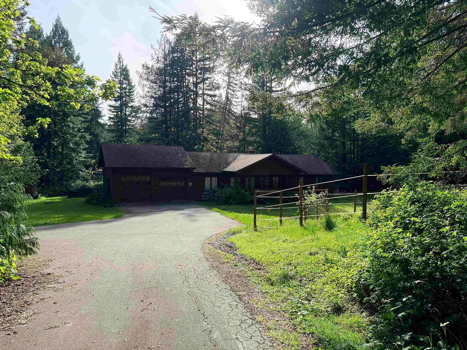 Front-and-side view of the house from the driveway, under the tree canopy.