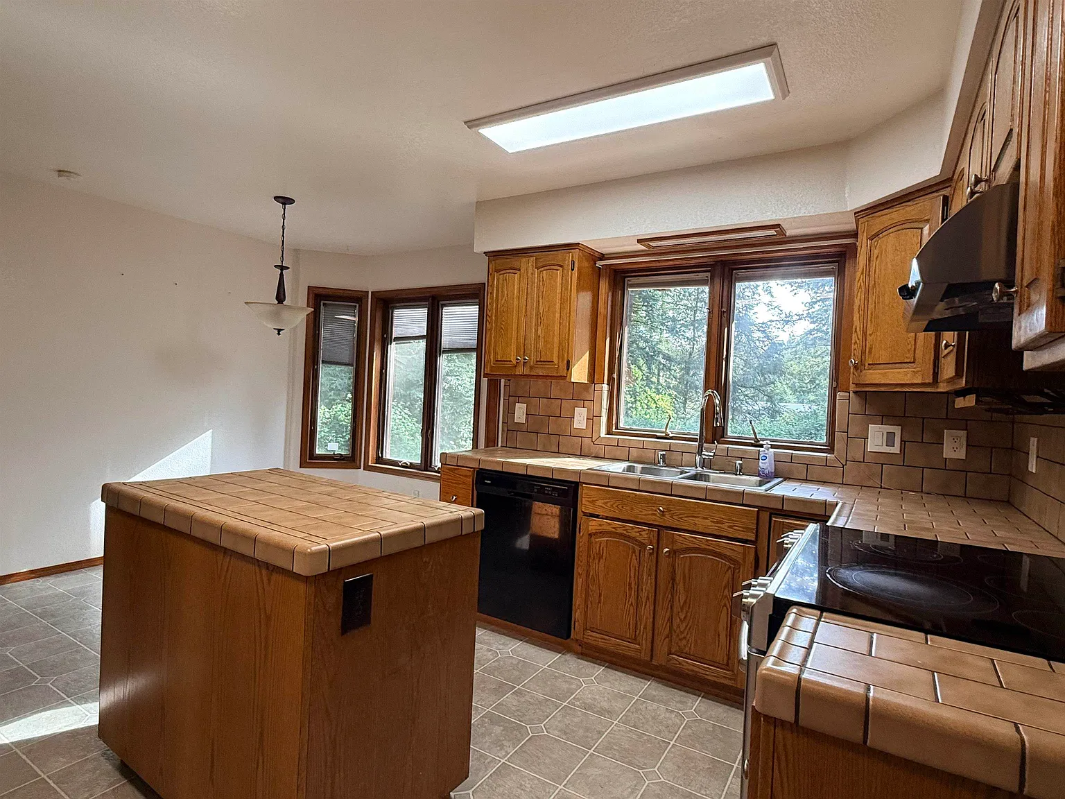 Kitchen with skylight, tile counters, and a window over the sink.